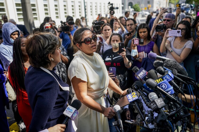 A woman speaks in front of dozens of microphones outside a federal courthouse