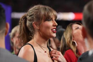 A picture of Taylor Swift's side profile. She wears a black sleeveless top, her hair in a braided ponytail and necklaces