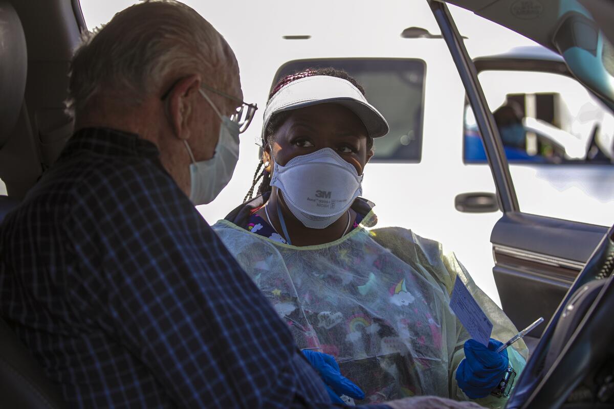 Travel nurse Reshicka Upshaw, wearing PPE, speaks with Robert Keler, 91, standing in the open door of his car.
