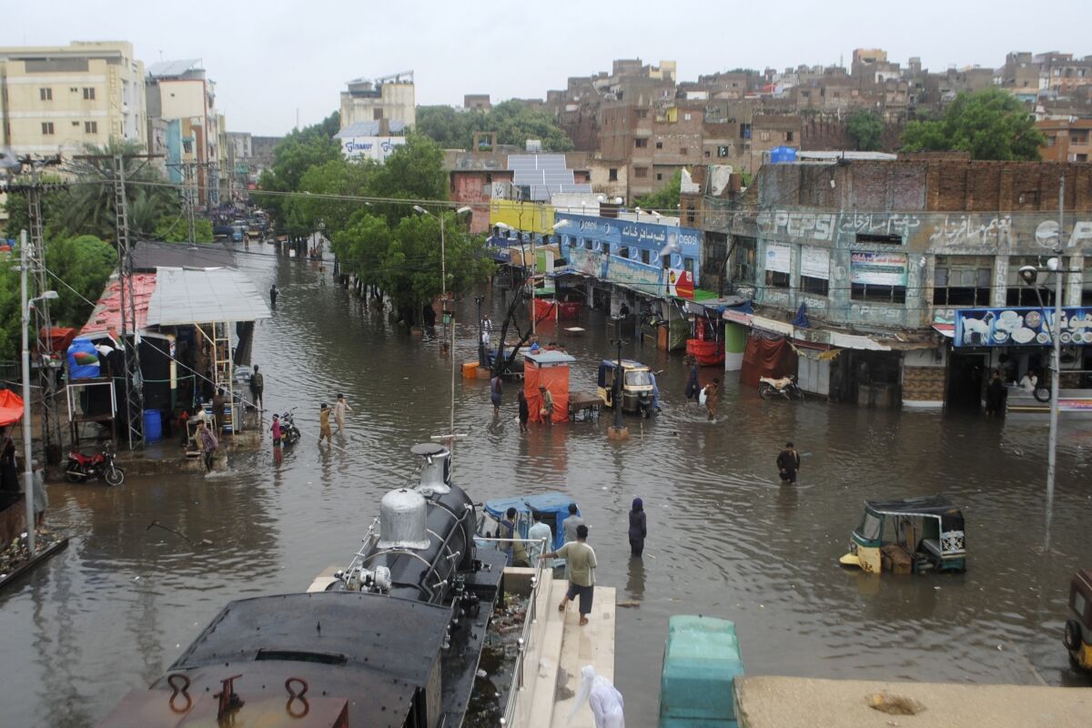 A view of people standing in floodwaters near a row of buildings and partially submerged vehicles