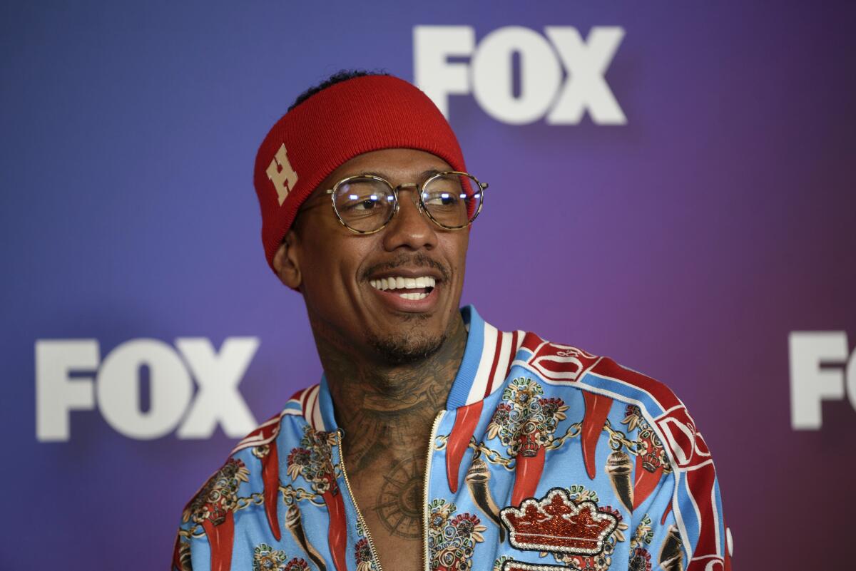 Nick Cannon wears a patterned jacket, glasses and a red sweatband