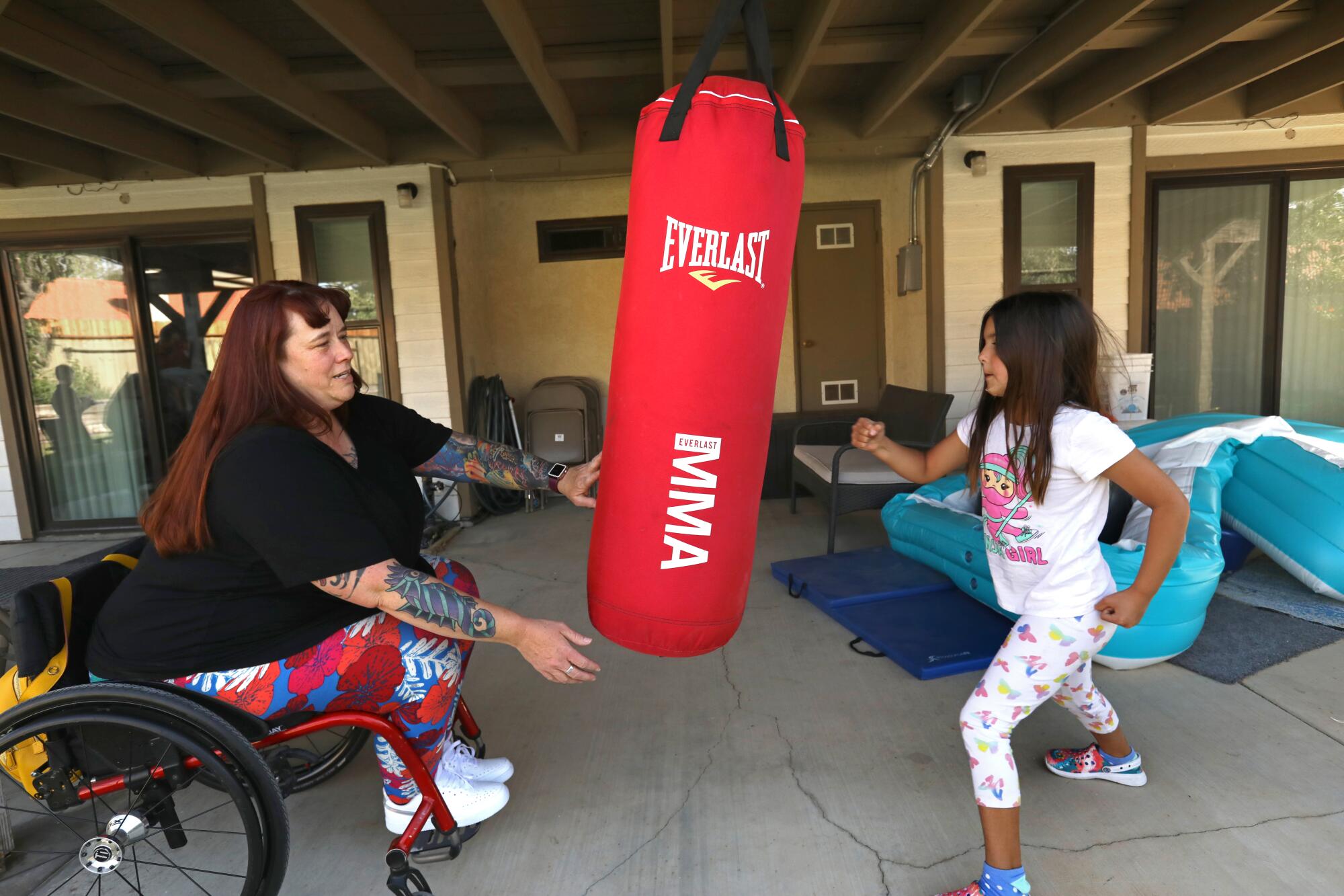 A woman sits in a wheelchair and holds a punching bag as she play with a young girl