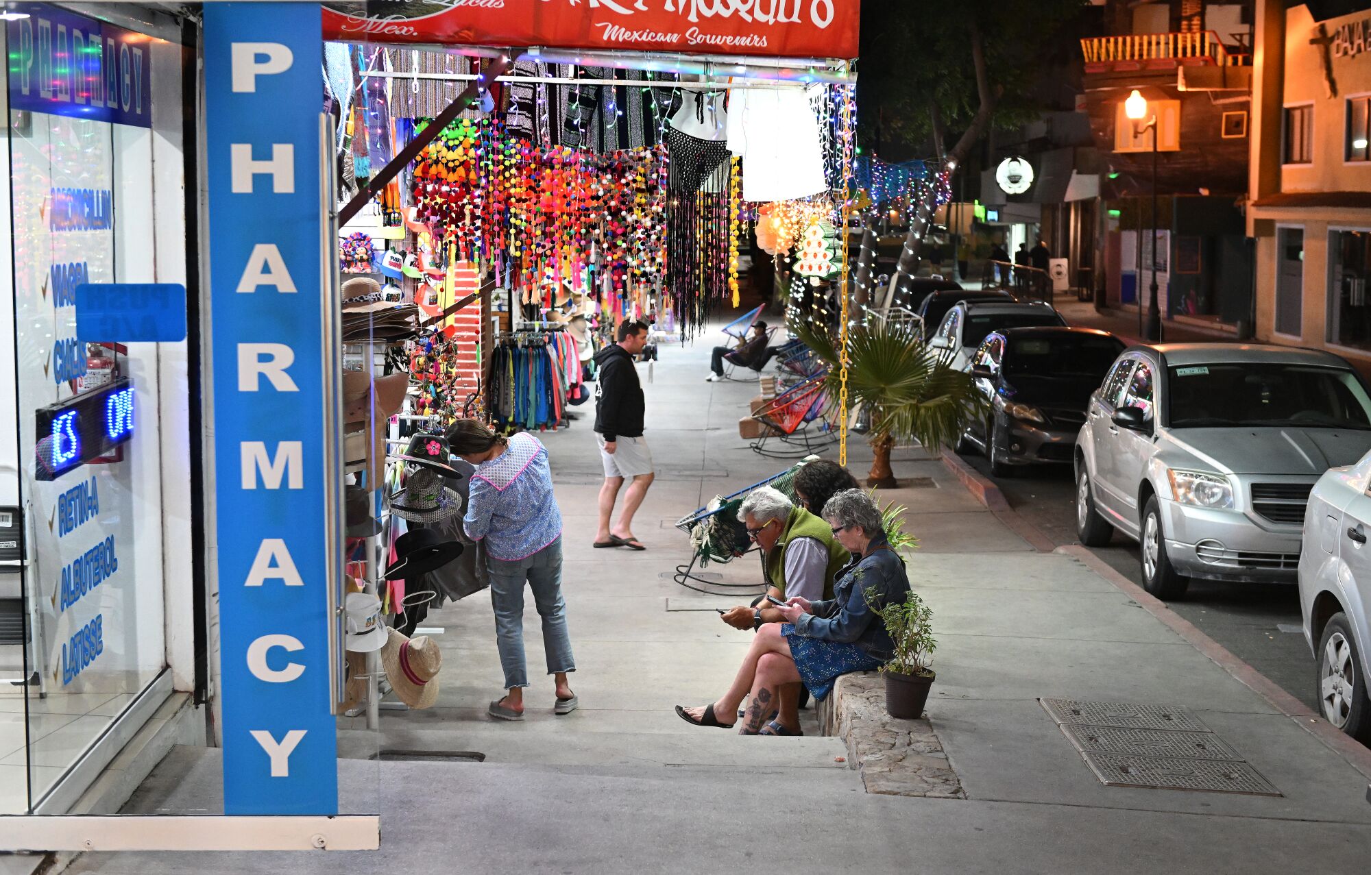 A street with shops. One has a vertical sign that says "Pharmacy."
