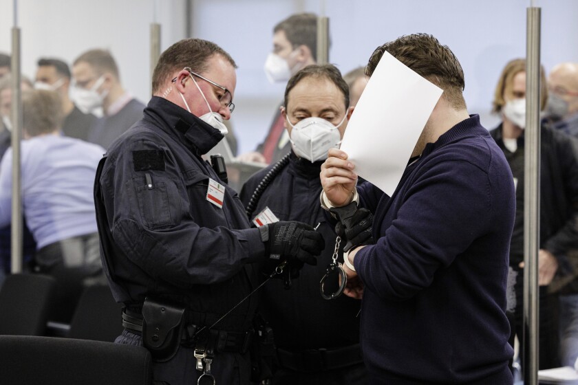 The defendant Rabieh R., right, hides his face as he is led into a courtroom of the Higher Regional Court in Dresden, eastern Germany on January 28, 2022 prior to the start of a trial over a jewellery heist on the Green Vault (Gruenes Gewoelbe) museum in Dresden's Royal Palace in November 2019. Six members of a notorious criminal gang, aged 22 to 28, go on trial in Germany on January 28 over the spectacular heist in which 18th-century jewels were snatched from the state museum in Dresden. They are accused of gang robbery and arson after the brazen night raid on The Green Vault museum on November 25, 2019. (Jens Schlueter/ Pool via AP)