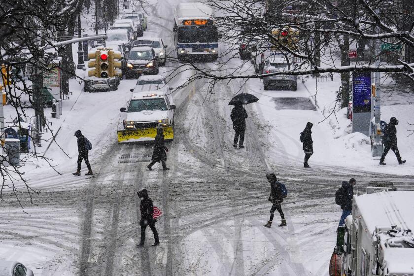 Pedestrians cross 71st Avenue as snow falls Thursday, Feb. 18, 2021, in the Queens borough of New York. (AP Photo/Frank Franklin II)