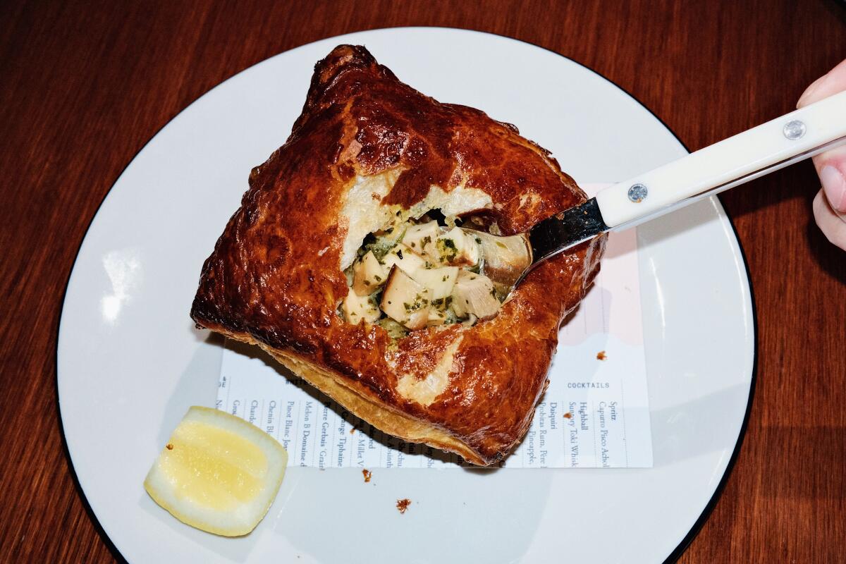 A spoon lifts abalone and mussels from the center of a pot pie with lemon on a white plate at Camélia in the Arts District