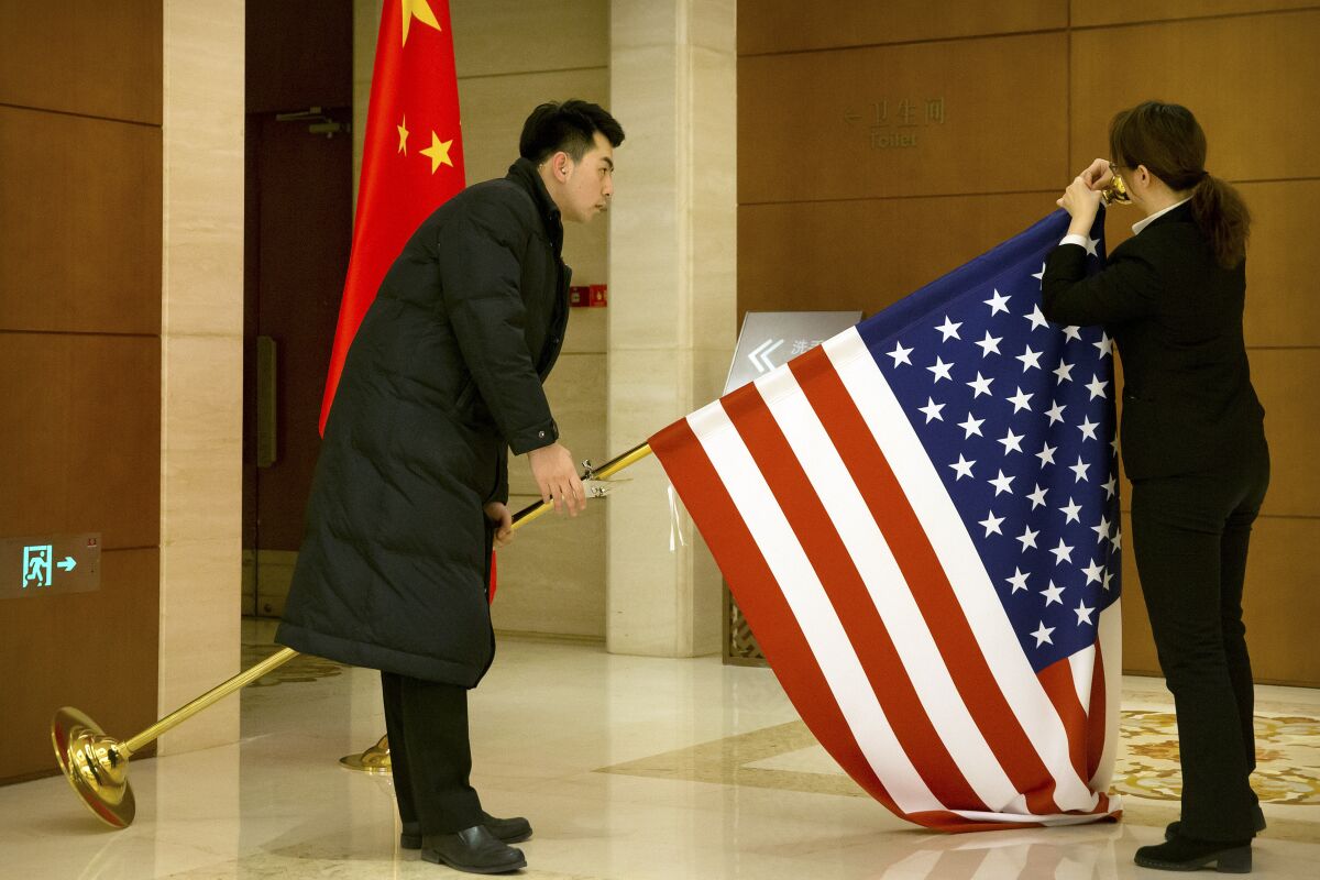 FILE - In this Feb. 14, 2019, file photo, Chinese staffers adjust a U.S. flag before the opening session of trade negotiations between U.S. and Chinese trade representatives at the Diaoyutai State Guesthouse in Beijing. China is delaying the renewal of press cards for at least five journalists working at four U.S. media outlets, an organization of foreign correspondents said Monday, Sept. 7, 2020 making them vulnerable to expulsion in apparent retribution for Washington's targeting of Chinese reporters working in the United States. (AP Photo/Mark Schiefelbein, Pool, File)