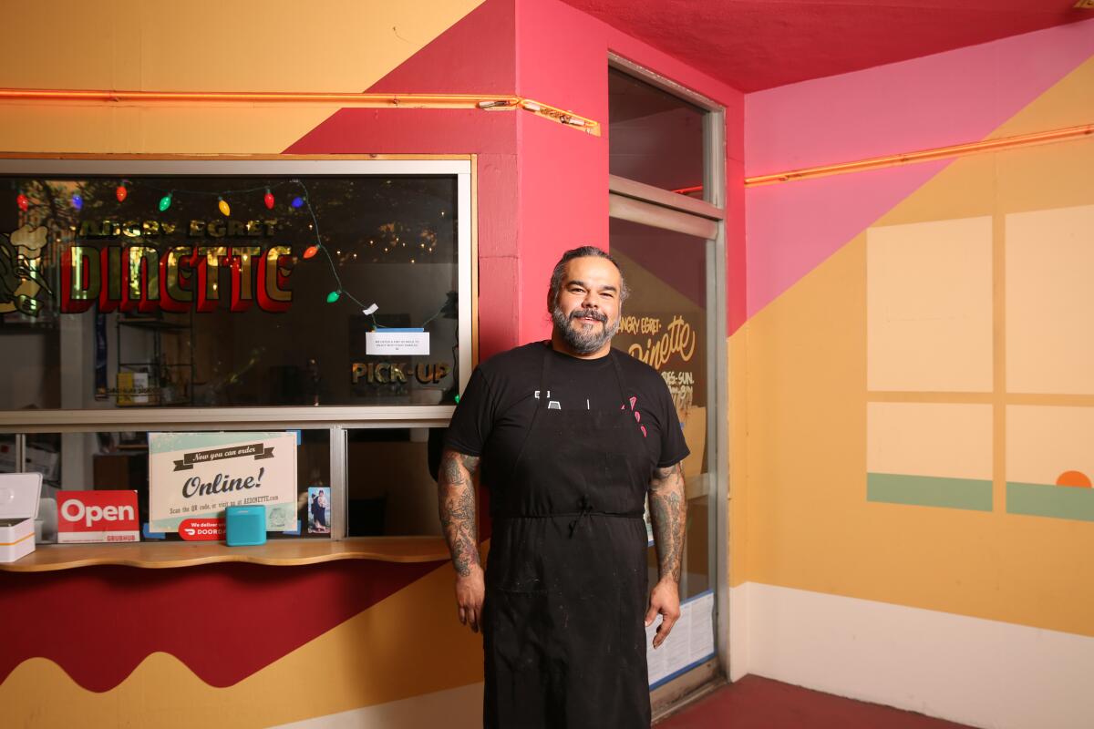 A bearded man dressed in black stands in a colorfully painted room