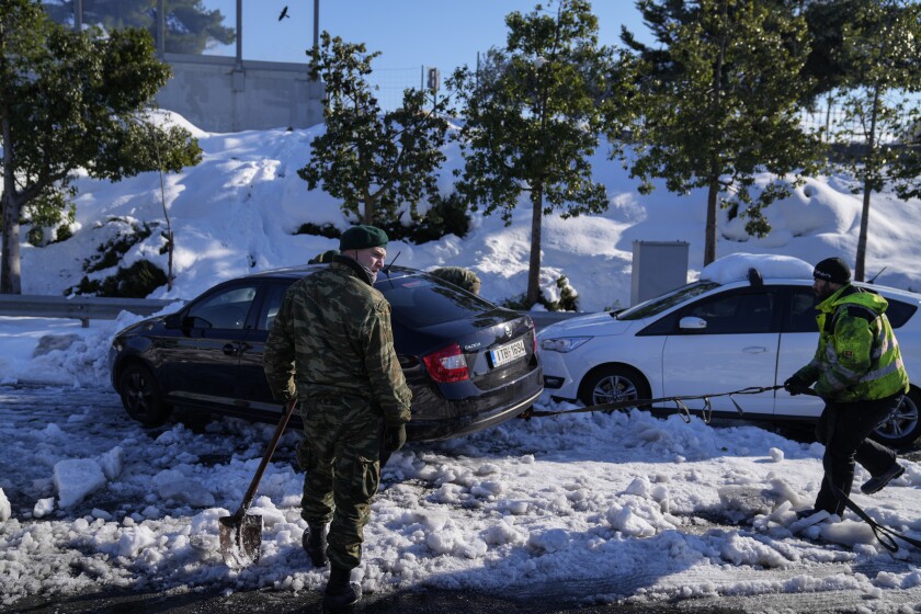 Greek soldiers try to free a vehicle stuck in snow on the Attiki Odos motorway, following Tuesday's heavy snowfall, in Athens, on Wednesday, Jan. 26, 2022. (AP Photo/Thanassis Stavrakis)