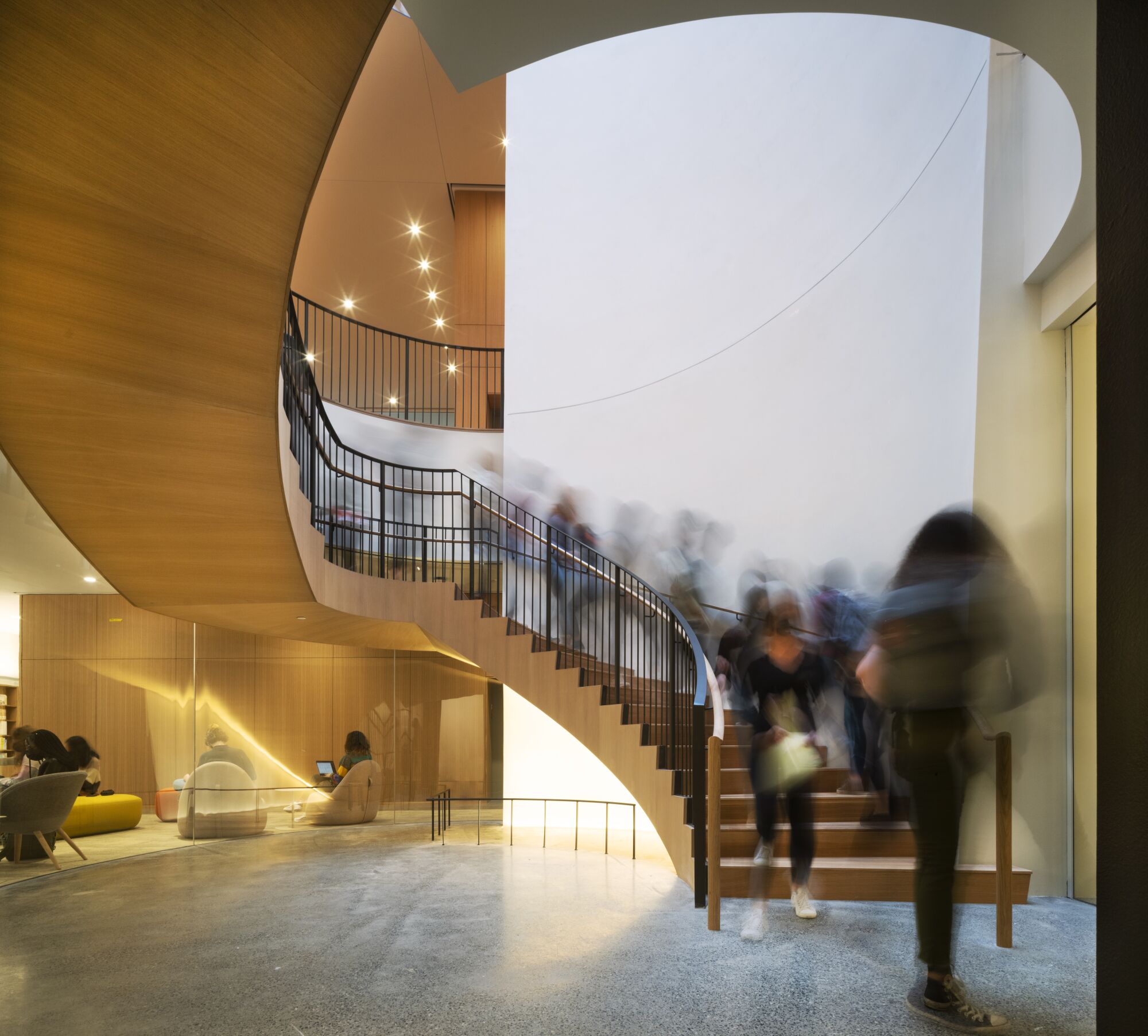 Blurred human figures descend a gently curving, wooden staircase.