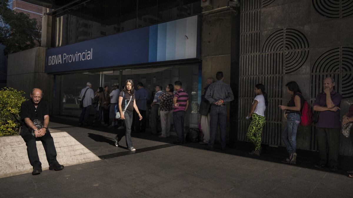 People line up to withdraw cash from an ATM in Caracas.