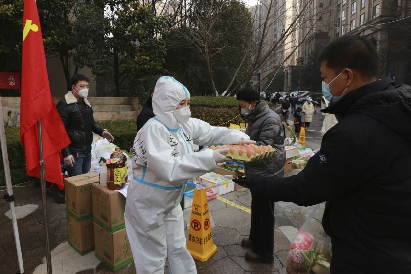 A community volunteer hands over eggs to a buyer at a temporary food store to provide supplies to residents outside a residential block in Xi'an city in northwest China's Shaanxi province Monday, Jan. 03, 2022. Authorities in the northern Chinese city of Xi'an say they can provide food, health care and other necessities for the roughly 13 million under an almost two-week old lockdown. But some residents describe difficulties obtaining supplies and frustration and the economic impact on the city that is home to the famed Terracotta warriors, along with major industries. (Chinatopix Via AP)