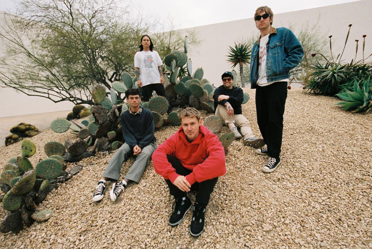 Five young guys in a band pose in a rock and cactus garden 