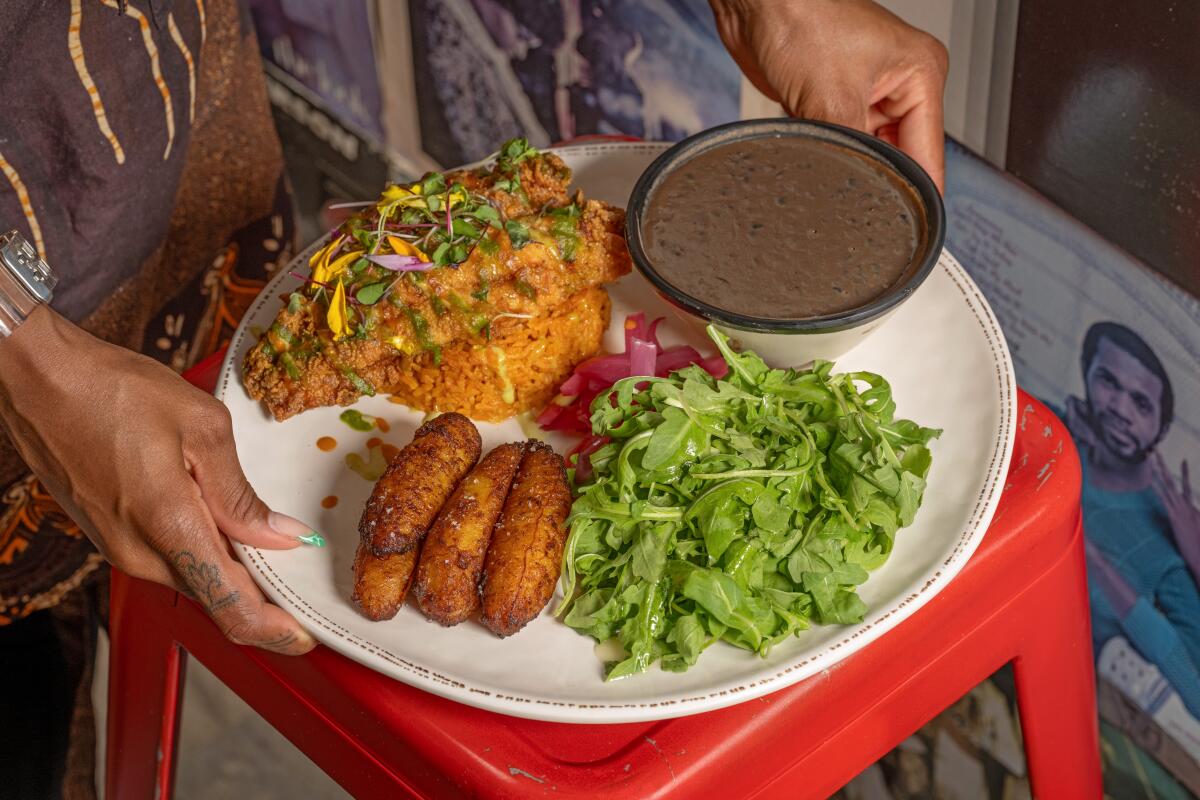 Two hands carry a jollof race platter with fried catfish at Two Hommes