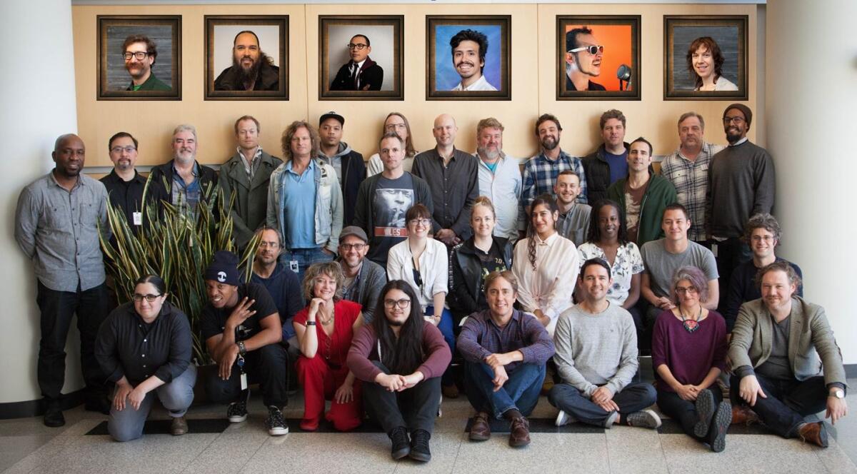 The team behind Pandora's Music Genome Project sits or stands in a group under framed photos of several people