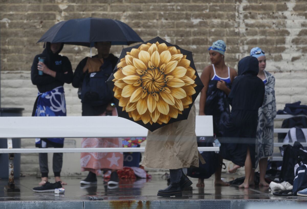 Swimmers duck under umbrellas as a heavy rain fall pounds the pool deck at Newport Harbor High.