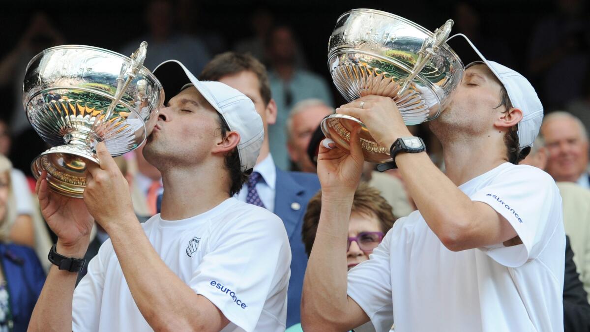Bob, left, and Mike Bryan lift and kiss their trophies after winning the Wimbledon doubles title in 2013.