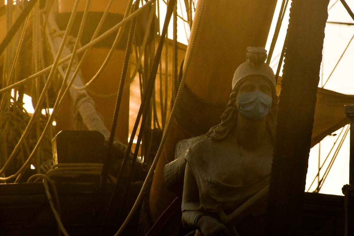 A female figure on a tall ship has a paper mask.