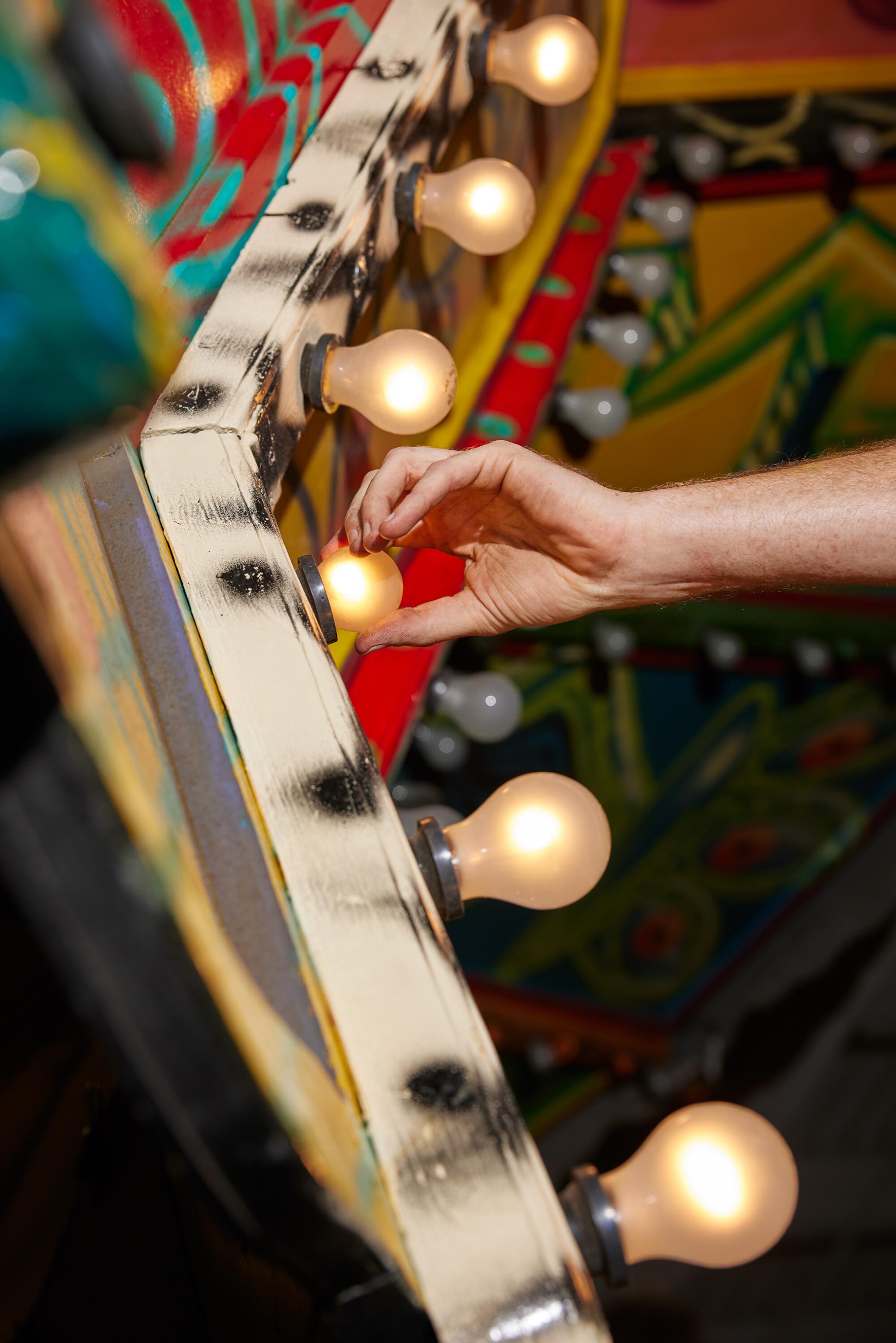 A hand screws in a light bulb on a carnival ride, seen in closeup
