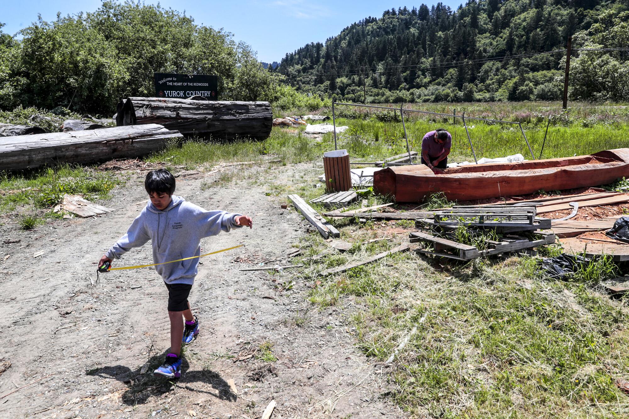 A Yurok boy plays while his father works on a canoe.
