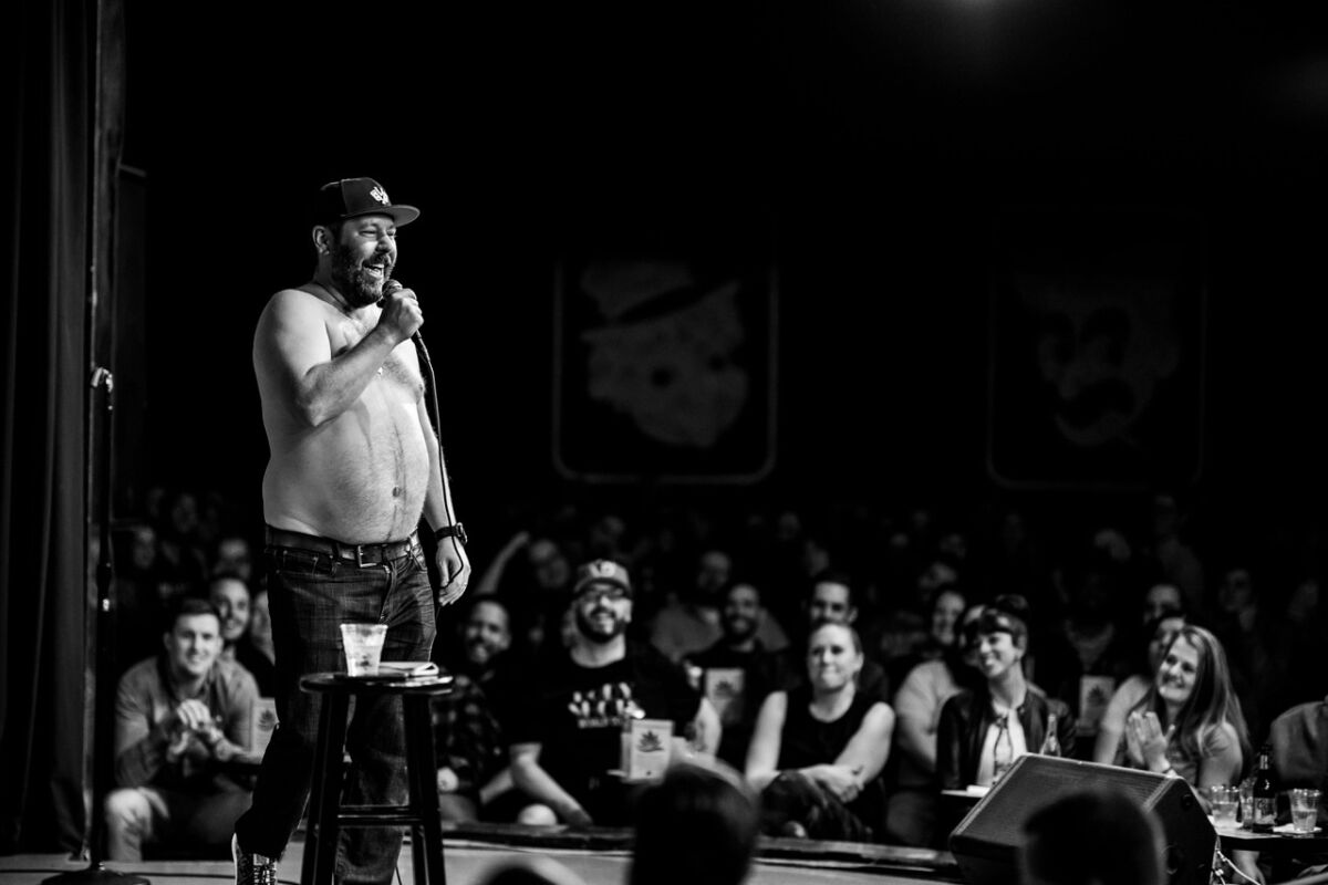 A black and white photo of a shirtless man doing stand-up 