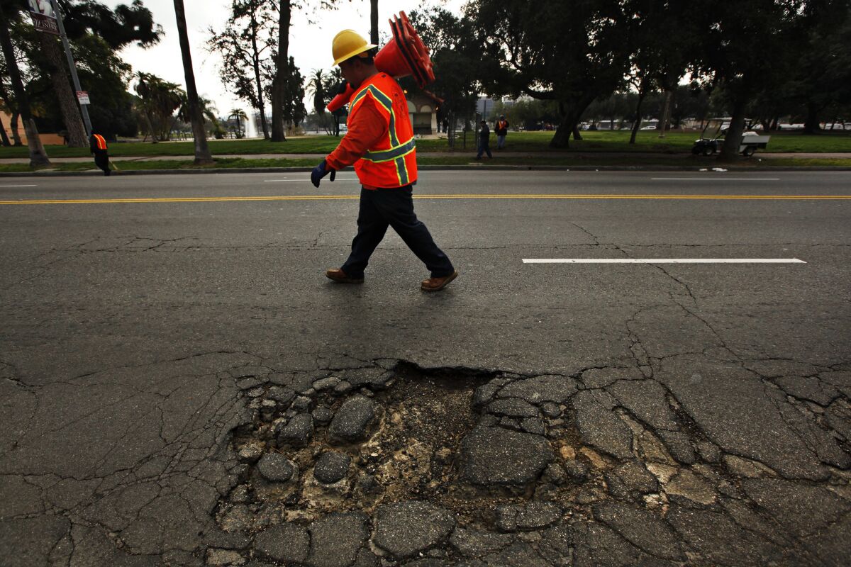 A Bureau of Street Services worker places cones on the road near a large pothole on Mission Road in Los Angeles.