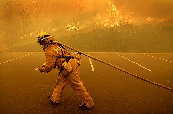 L.A. County Firefighter Ron Hughes drags hose to protect a commercial building along Agoura Road as a brush fire burns in the Calabasas and Agoura Hills area.