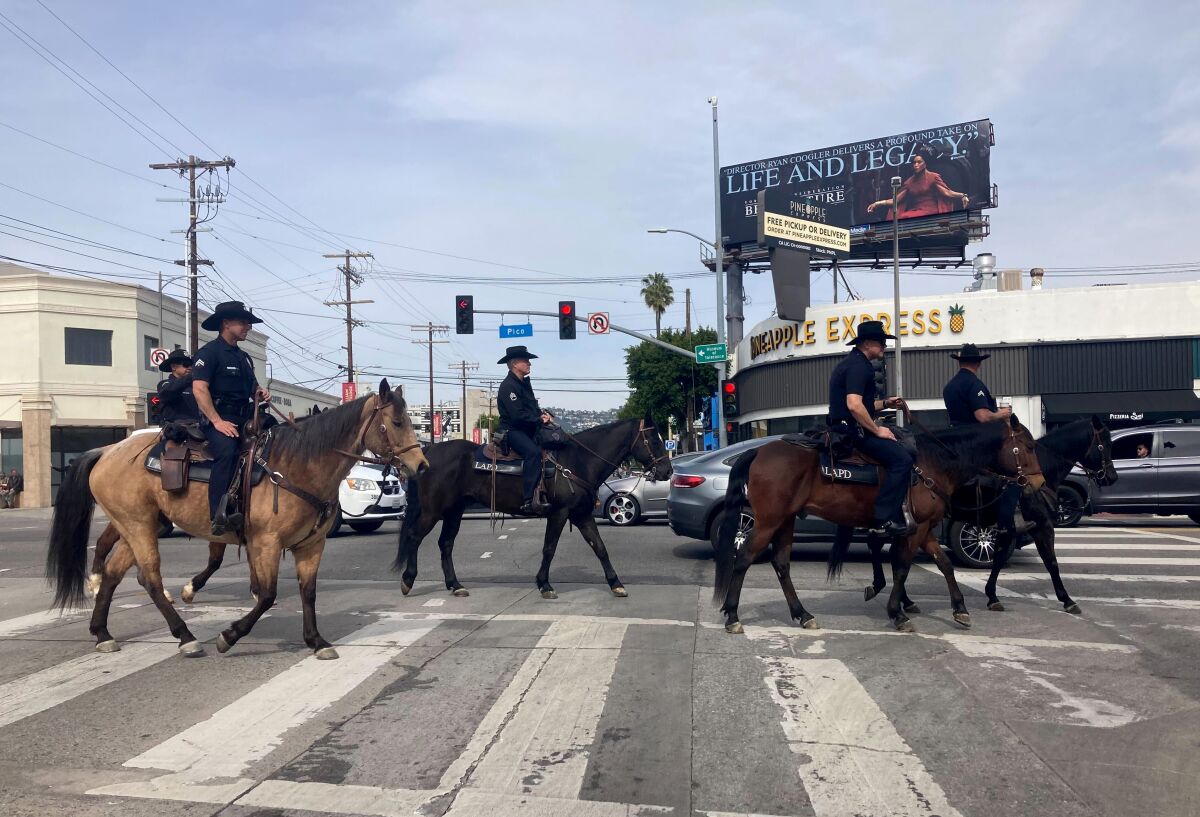 Police officers on horseback cross a city intersection.