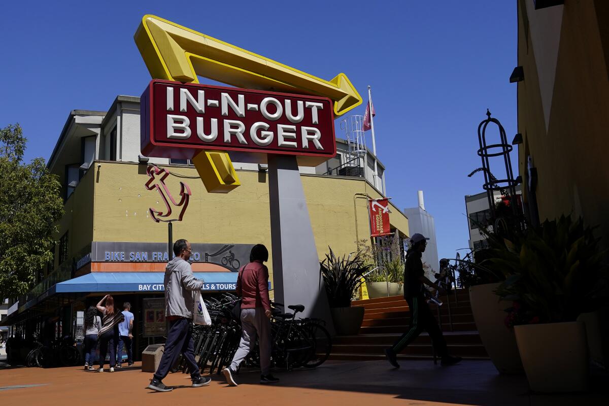 Pedestrians walk below an In-N-Out Burger restaurant sign in San Francisco.