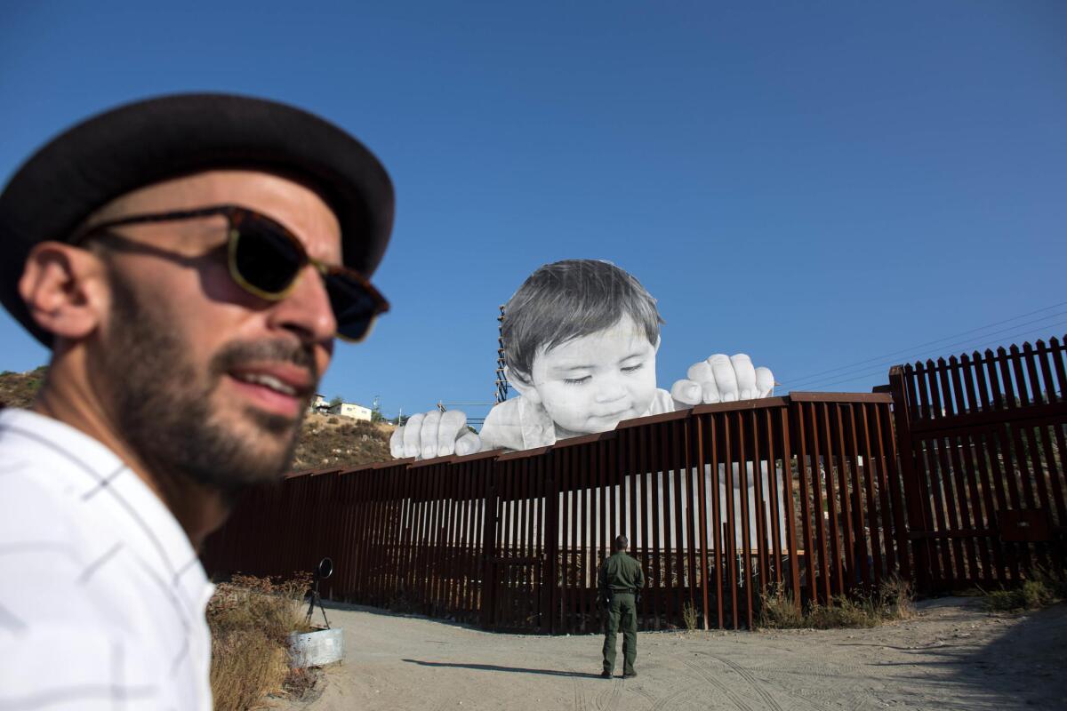 French artist JR, pictured near his artwork on the U.S.-Mexico border in Tecate, Calif., will be speaking about immigration Thursday in Los Angeles.
