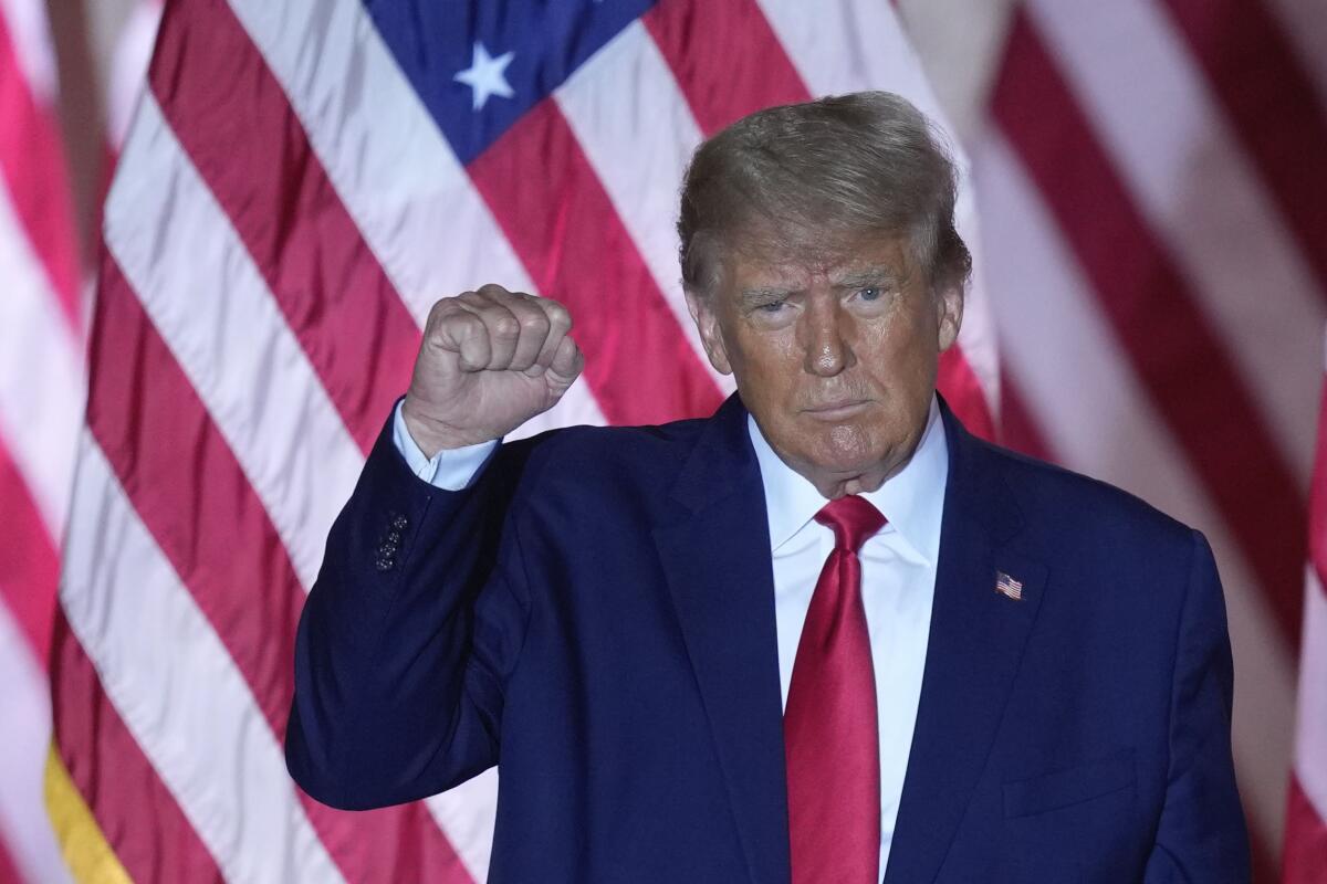 Former President Trump standing in front of a large American flag, raising his fist