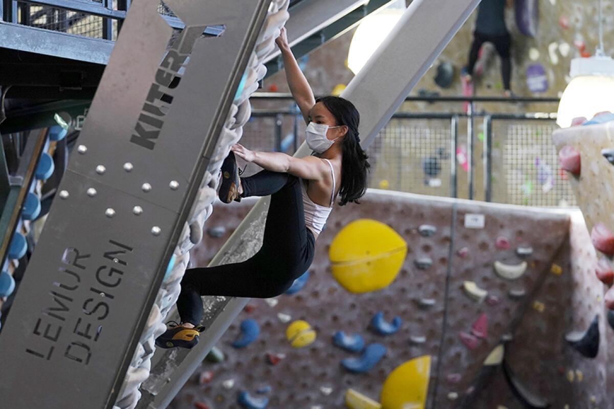 A masked woman climbs an indoor rock wall.