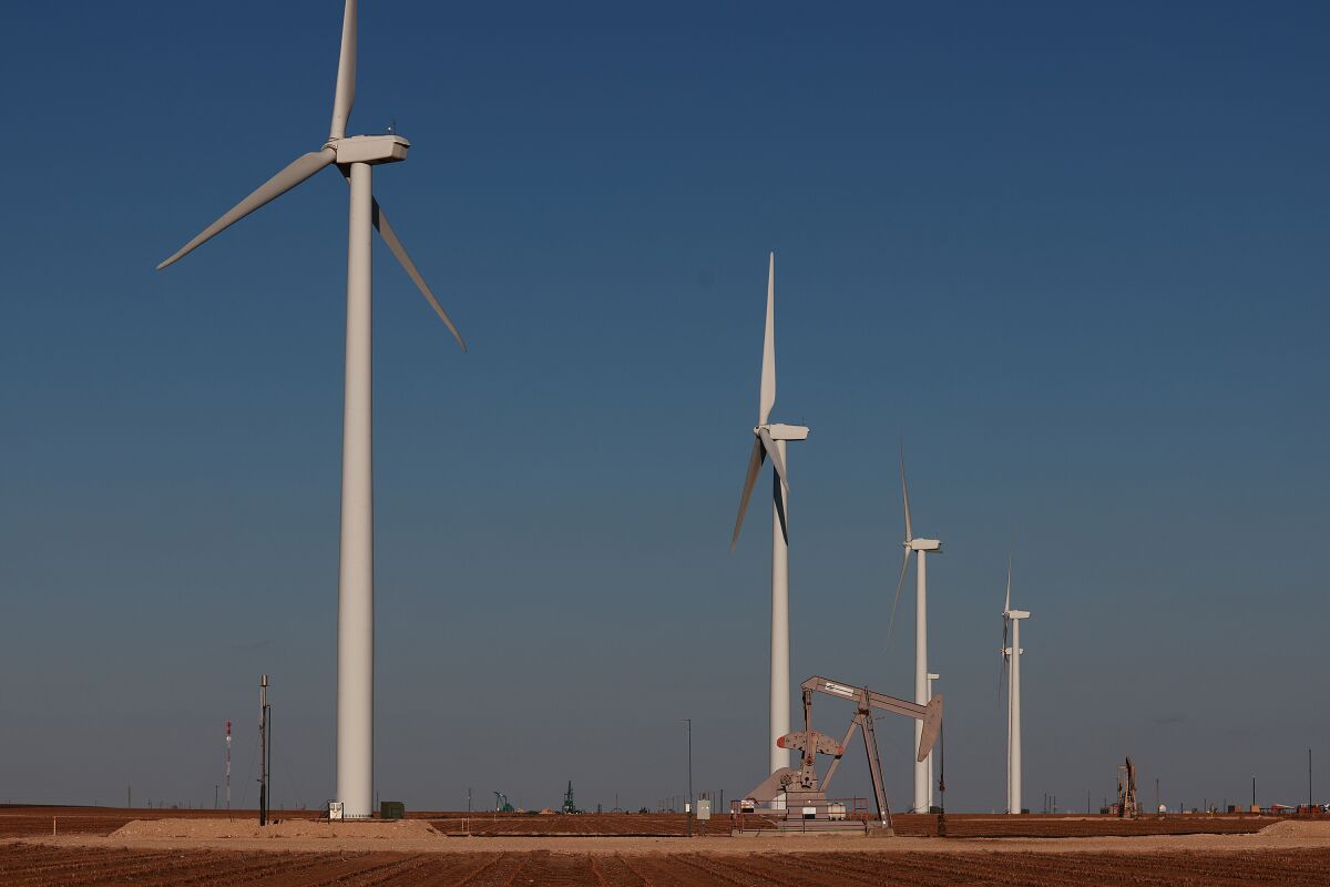 An oil pumpjack works near wind turbines in the Permian Basin oil field in Stanton, Texas.