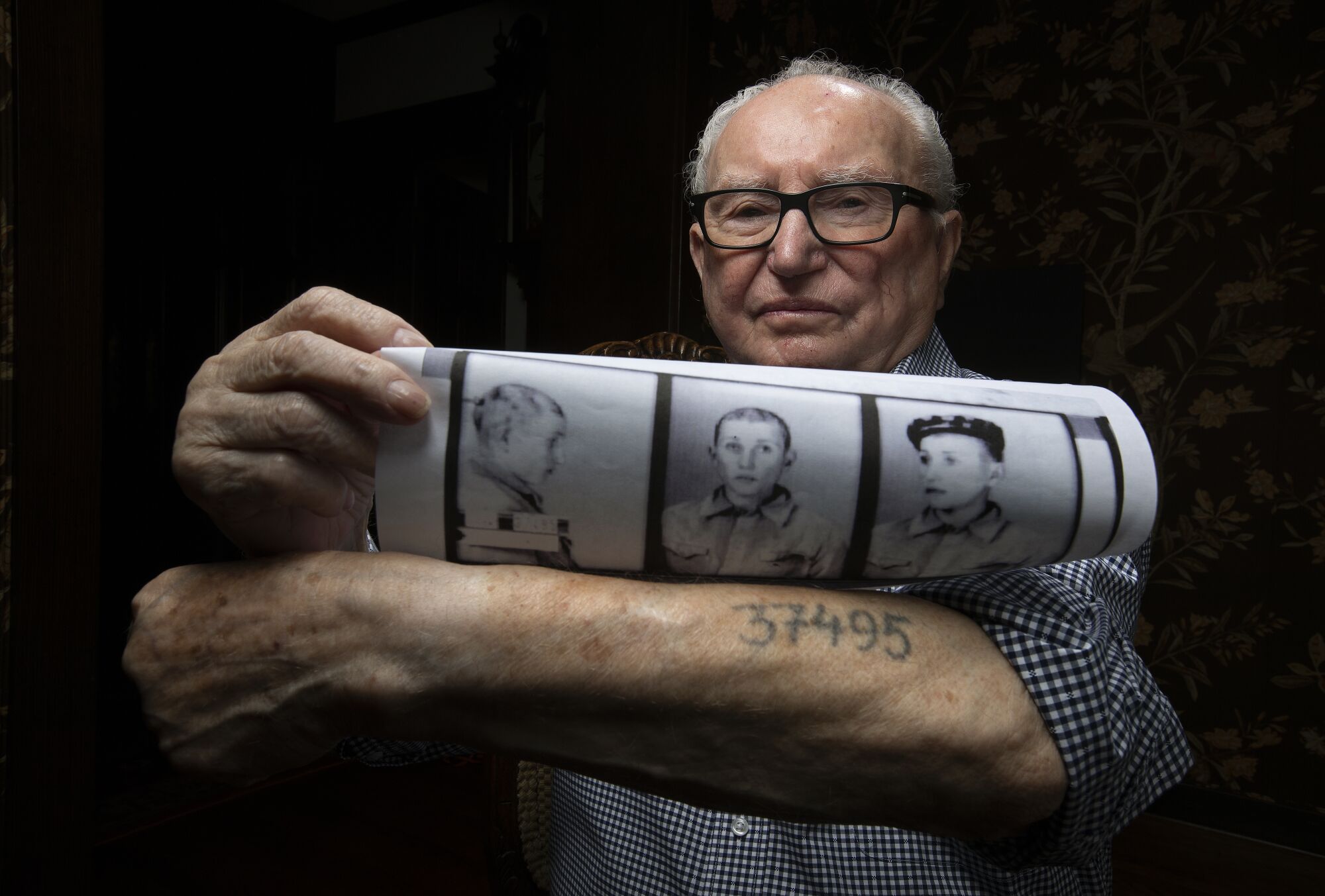 Ralph Hakman shows prisoner photos of himself from 1942, along with his prisoner number that was tattooed on his left arm.