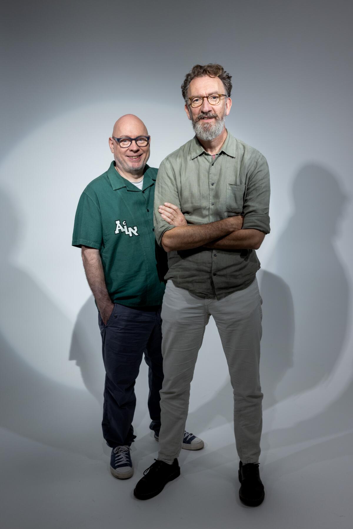 A bald man in a green shirt (Gary Clark) stands behind a tall, bespectacled man with a graying beard (John Carney)