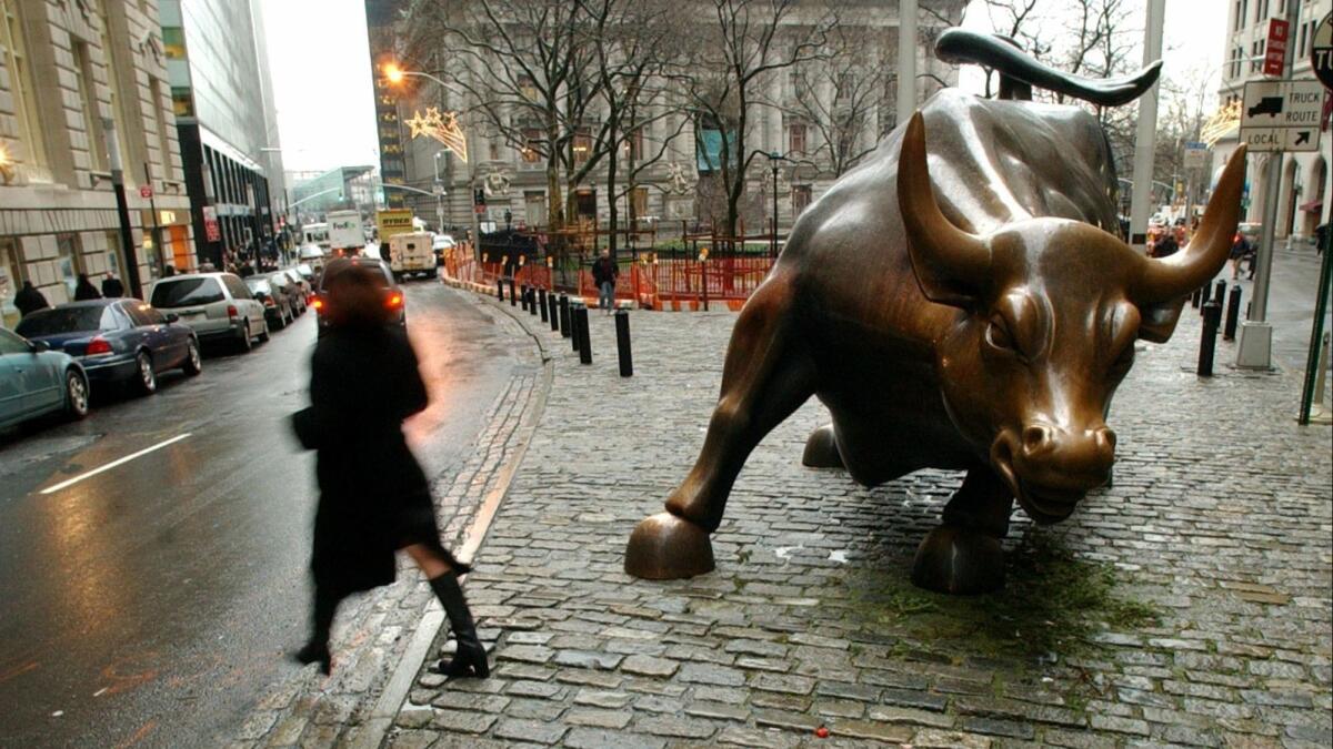 People pass the statue of the bull near Wall Street in New York.
