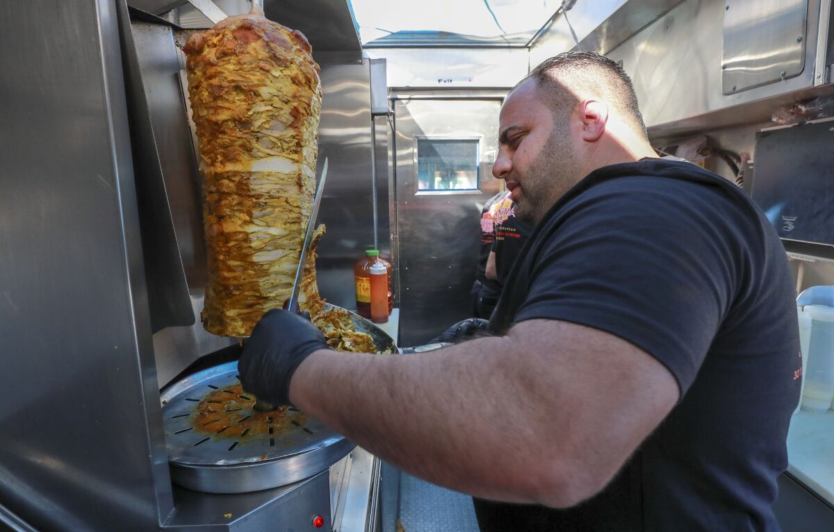 Bryan Zeto, owner of the Shawarma Guys food truck in South Park, carves off chicken shawarma shavings for a customer.