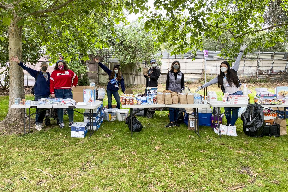 Volunteers with SELAH Neighborhood Homeless Coalition stand behind a table full of food and other items