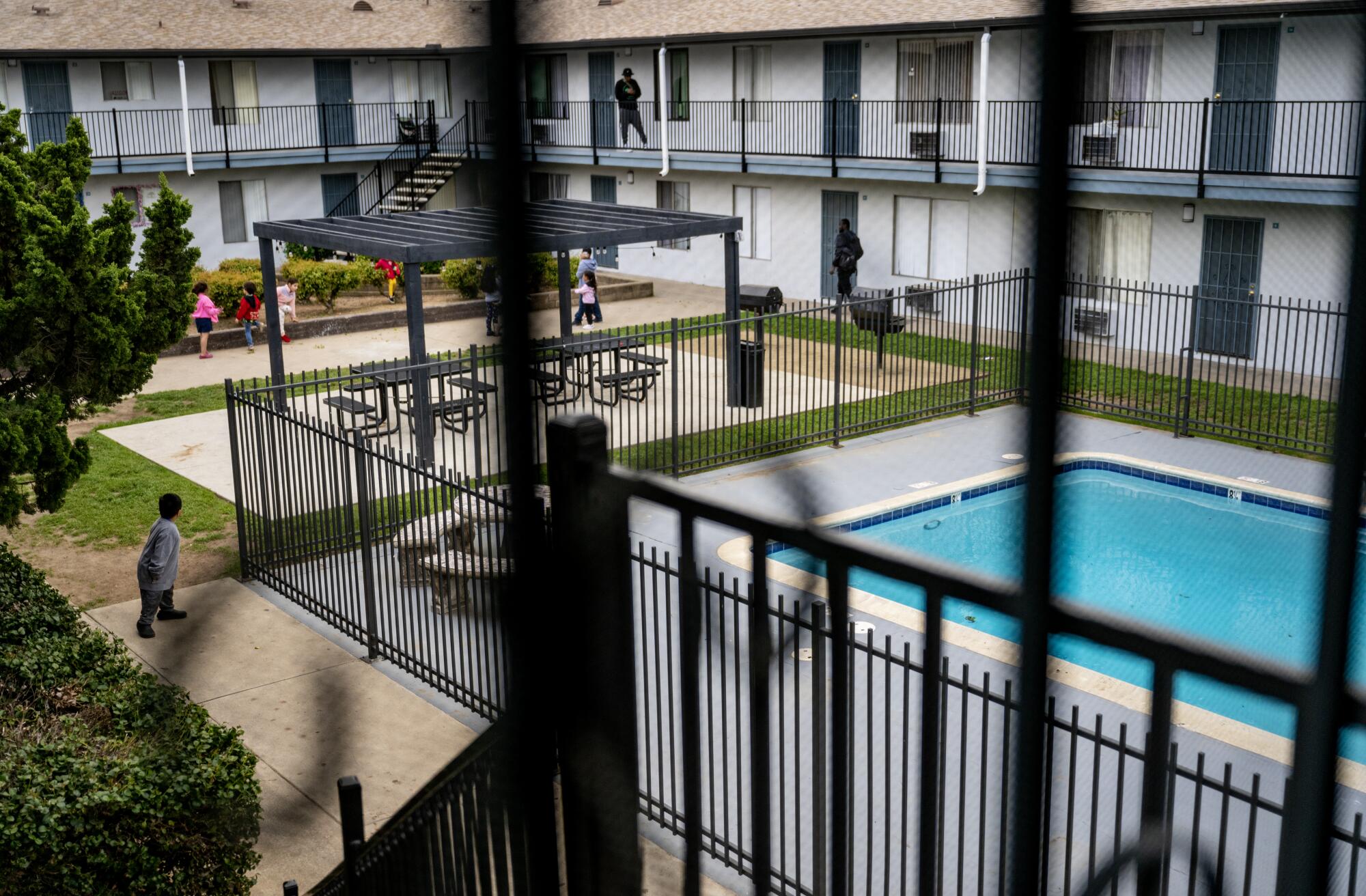 Children play outside a fenced pool.