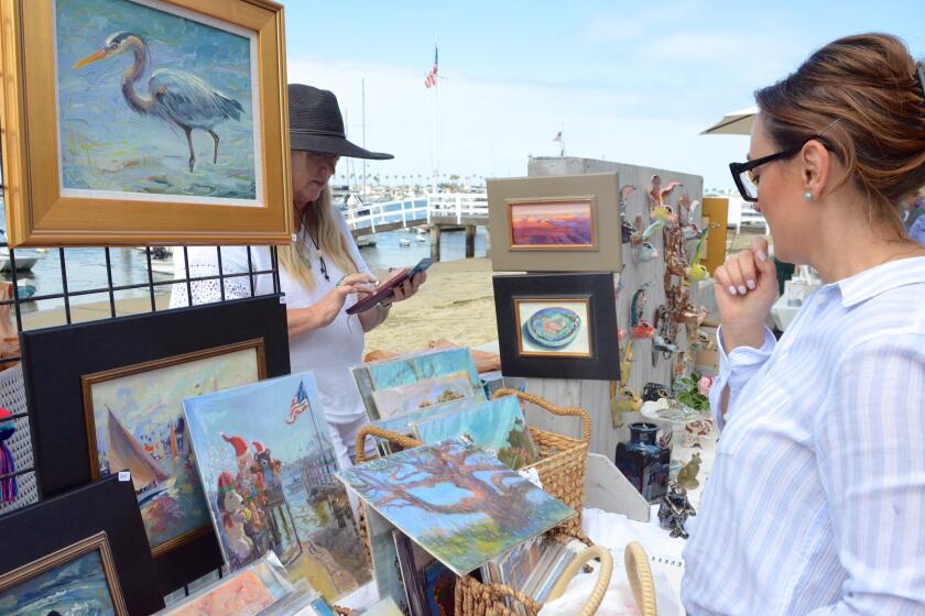 Diana Johnson admires her purchase as artist Kirsten Anderson tallies up the total at the Balboa Island ArtWalk.