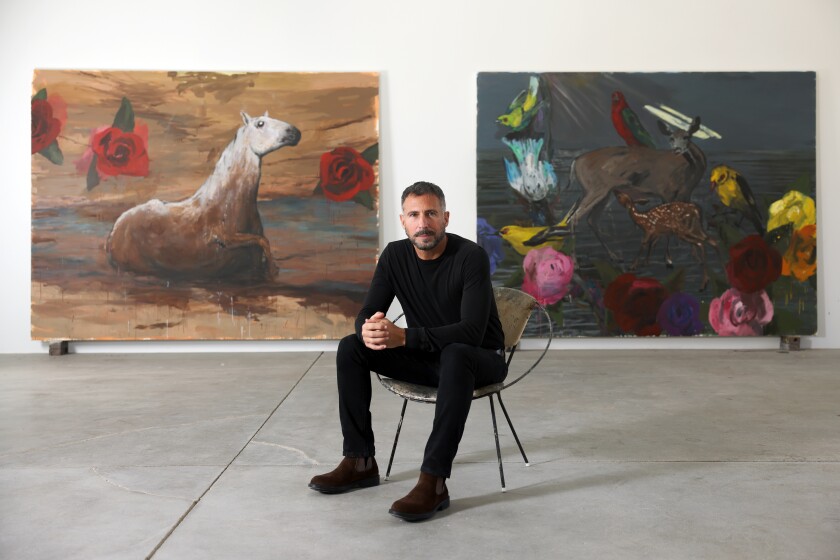 A man sits on a chair in a room with white walls; two large paintings are in the background.