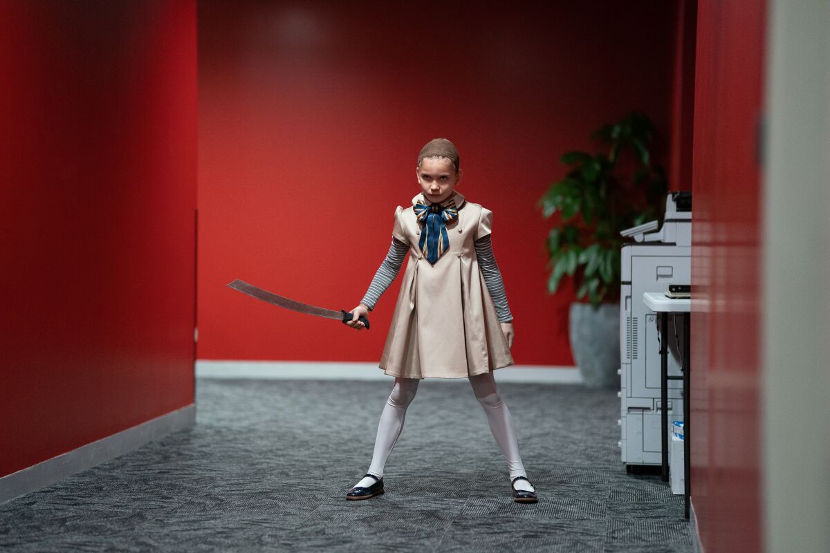 A girl in a dress and holding a long knife stands in a hallway in "M3GAN."