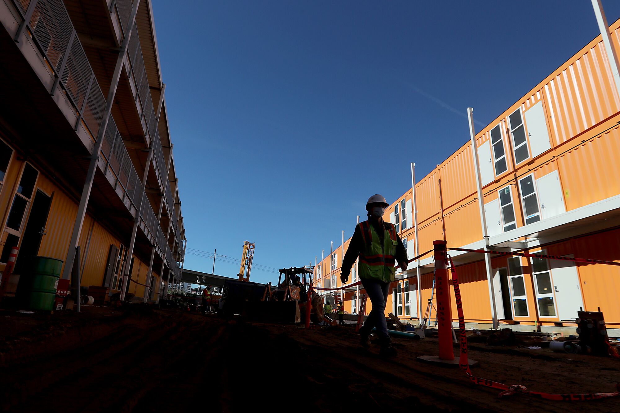 A worker in a hard hat and high-visibility vest walks in between housing built from shipping containers.