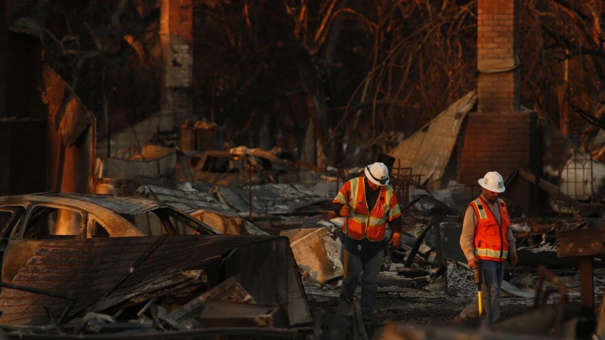 PG&E workers make their way through the fire-ravaged Coffey Park neighborhood in Santa Rosa on Oct. 14, 2017. The Northern California utility faces billions of dollars in payments for the role its equipment played in sparking the region's fires last year.