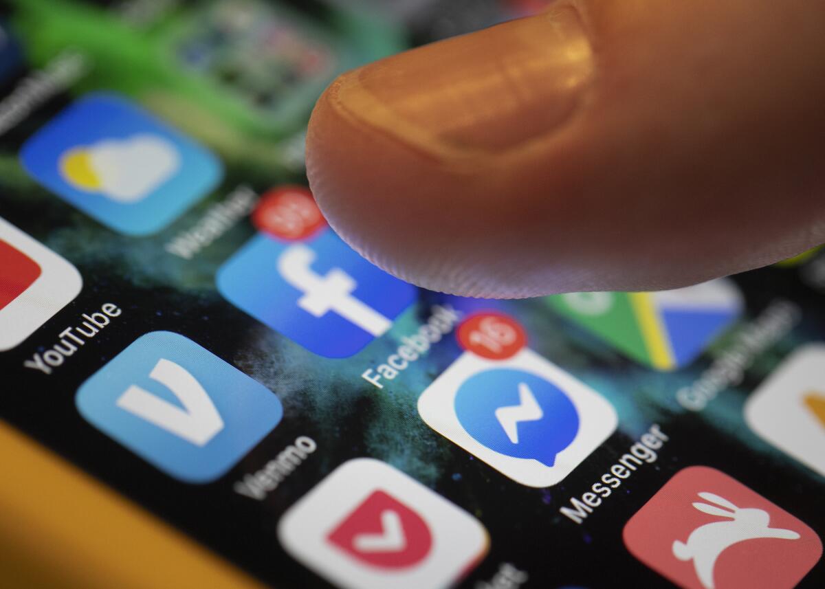 A closeup of a finger selecting the Facebook app icon on an iPhone screen. 