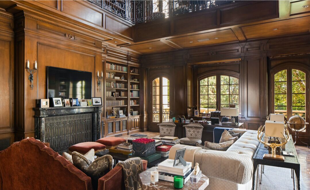 The wood-paneled library with shelves of books and seating with windows overlooking greenery.