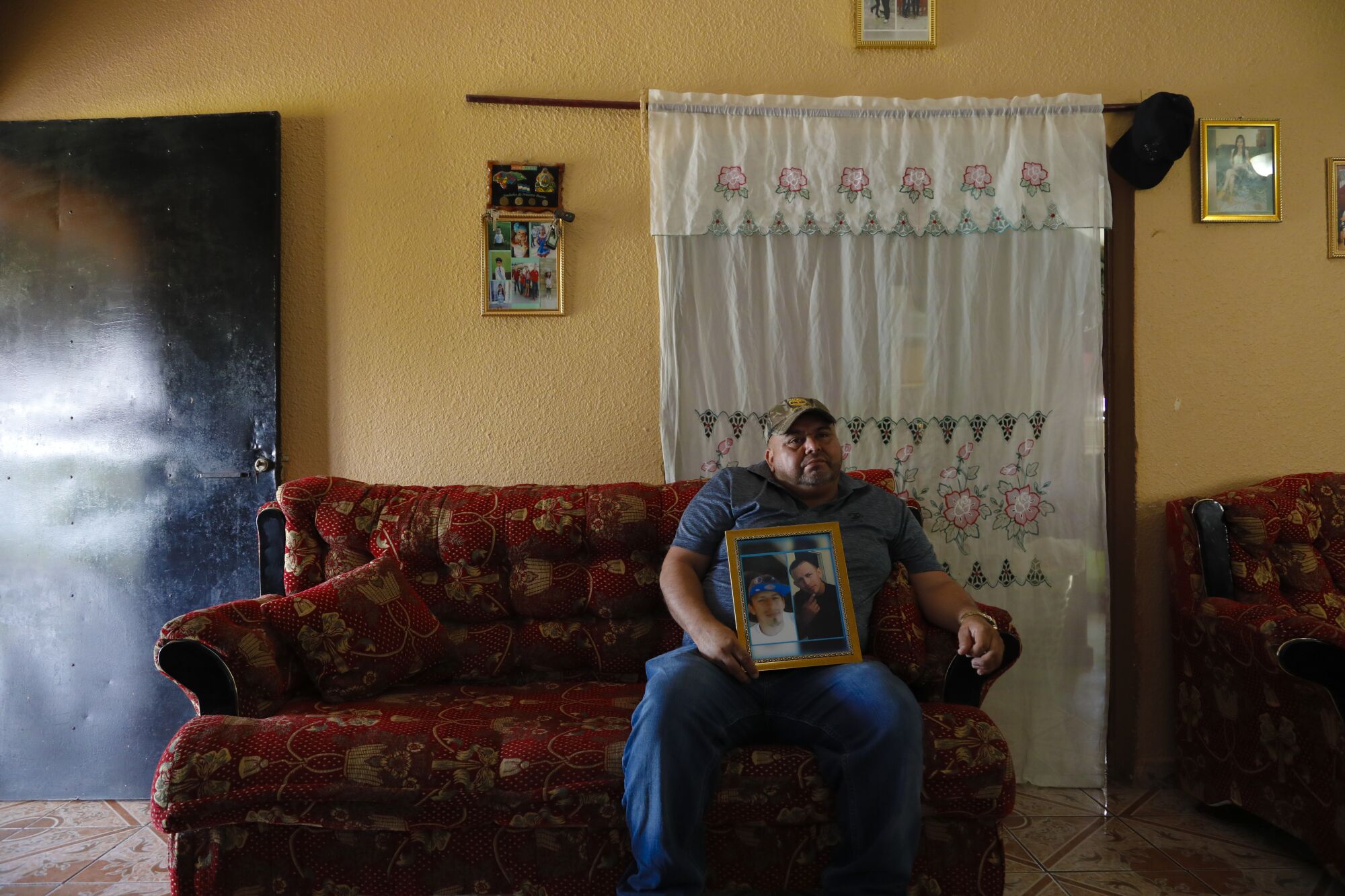 Alex Diaz Zavala sits on the sofa in his home in Honduras holding a photograph of his son