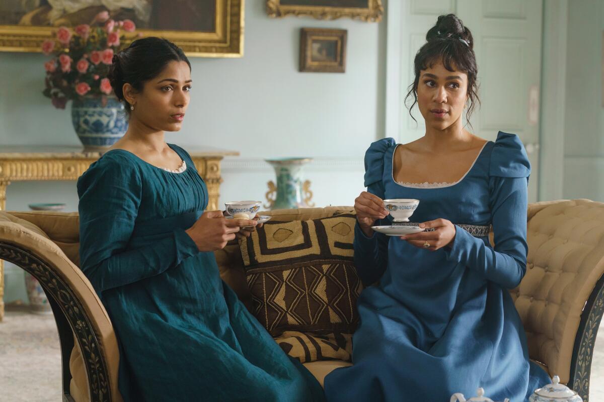 Two Regency-era in blue dresses drinking tea