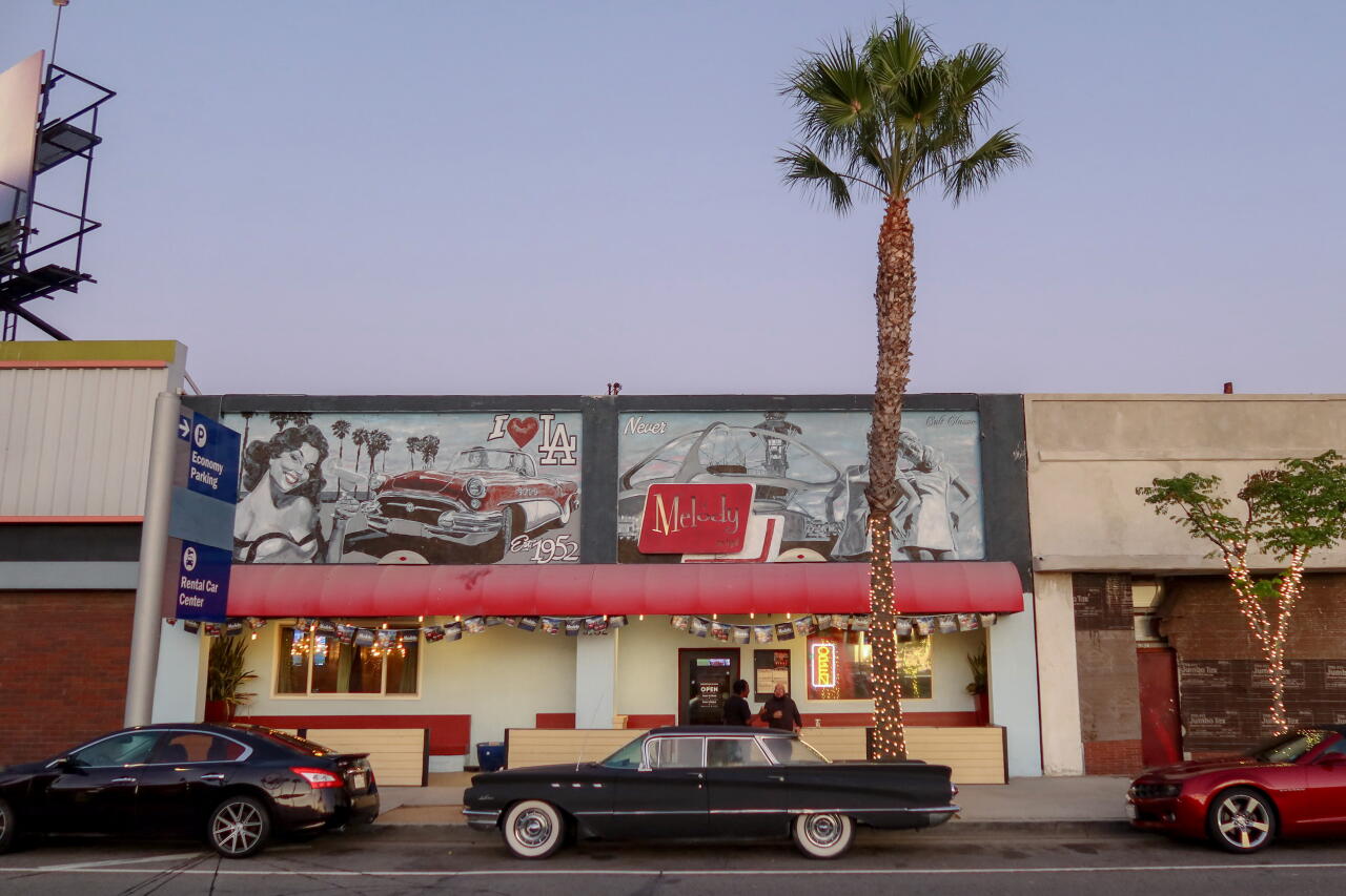 Cars parked in front of one-story buildings.