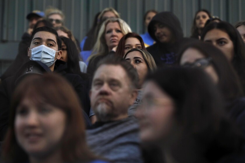 A fan at a UCLA women's softball game wears a mask in a crowd of maskless people
